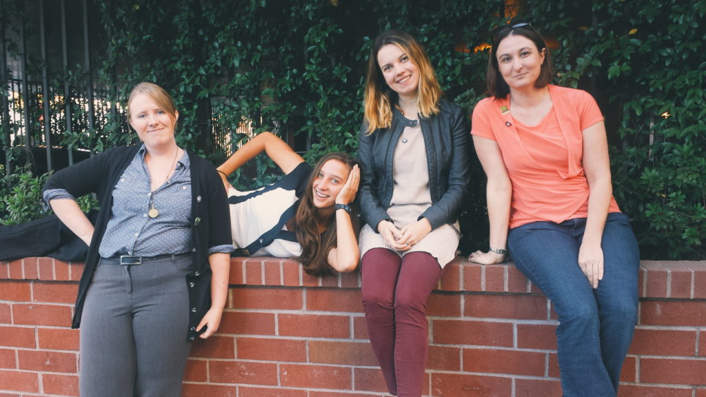 an image of four ladies sitting together on a waist high red brick wall